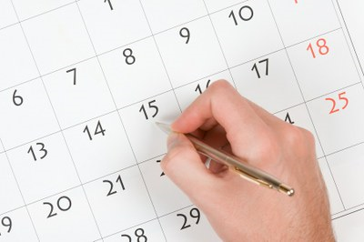 Imagem mostra mão humana segurando caneta apontando para um calendário 