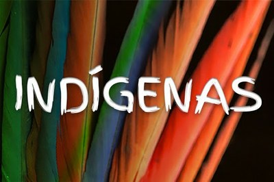 #PraCegoVer #PraTodosVerem: Arte em formato retangular exibe a palavra "Indígenas", na cor branca, sobre fundo com penas coloridas comumente utilizadas em artesanatos indígenas
