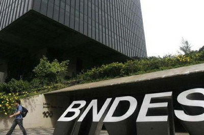A foto apresenta uma parte da fachada do prédio do BNDES com a inscrição "BNDES".