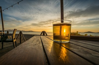 #Paratodosverem: Imagem mostra copo de cerveja sobre uma mesa na orla de uma praia ao fim da tarde