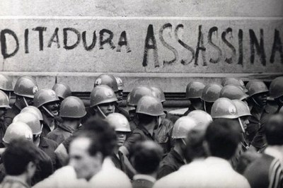 #Paratodosverem: Imagem mostra foto histórica na qual soldados estão reunidos em frente a um muro com a pichação "ditadura assassina"
