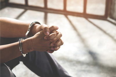Pessoa sentada no chão de cela com as mãos algemadas