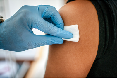 Imagem de profissional da saúde limpando área do braço de outra pessoa, preparando para aplicação de vacina