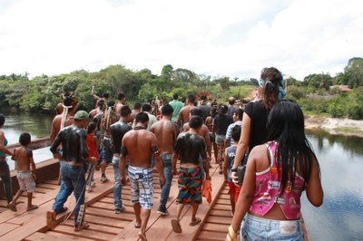Foto mostra indígenas caminhando sobre uma ponte de madeira