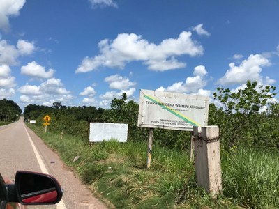 Foto mostra trecho de estrada com placa branca que indica a entrada da terra indígena Waimiri Atroari