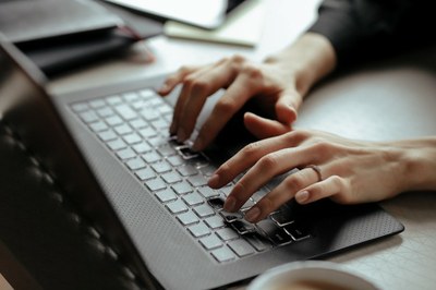 #ParaTodosVerem. Mãos de uma mulher digitando em um computador de cor cinza.