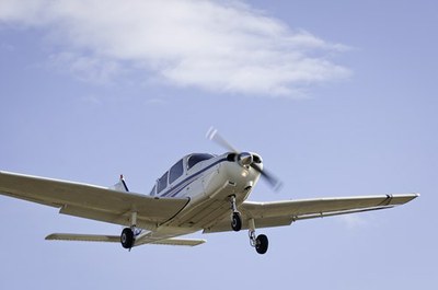 Avião monomotor em voo, ao fundo o céu com uma nuvem.