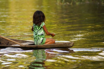 #pracegover foto mostra criança de costas em canoa em rio da amazônia