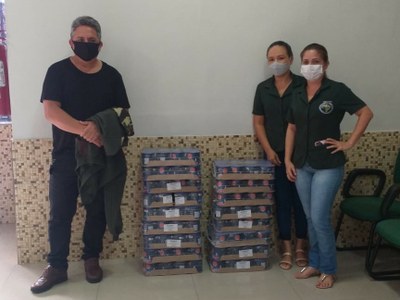 foto mostra servidor do MPF e representantes de instituição recebendo doação de 18 caixas de leite com café em lata. Todos usam máscara. 