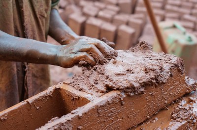 Foto mostra duas mãos trabalhando na produção de tijolo de argila