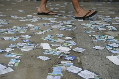 foto mostra material de campanha espalhado pelo chão, enquanto pessoa caminha usando chinelos pretos