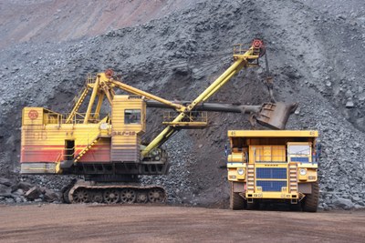 foto mostra uma escavadeira e um trator amarelos próximos a uma montanha de terra e minério.