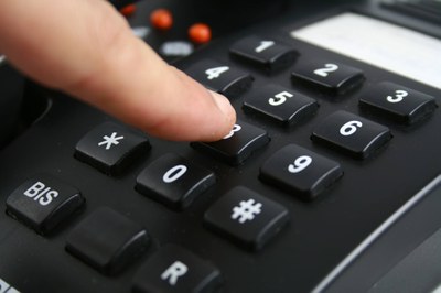 #pracegover foto mostra pessoa teclando números em um telefone fixo preto