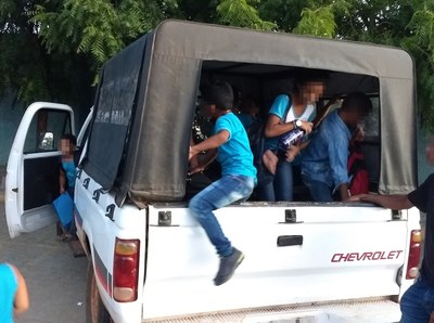 Foto de crianças uniformizadas sendo transportadas na caçamba de caminhonete