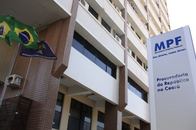 Foto da sede do MPF em Fortaleza. Em primeiro plano aparecem as bandeiras do Brasil e do Ministério Público, além de uma placa com a marca da instituição. 