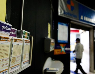 Foto interna de uma casa lotérica, tendo em primeiro plano cartelas para jogos lotéricos