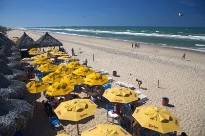 Imagem mostra a Praia do Futuro com quiosques e barracas de praia com guarda-sóis amarelos e, ao fundo, o mar.