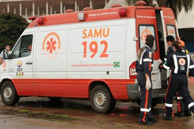 Foto de uma ambulância do SAMU. Três profissionais abrem a porta traseira do veículo 