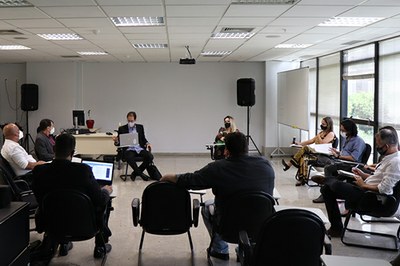 Foto da reunião realizada em uma sala com janelas grandes e os participantes sentados em cadeiras em um círculo.