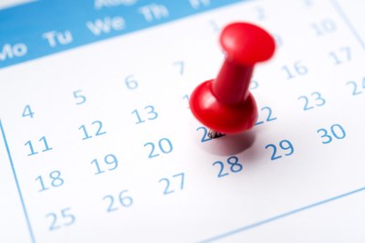 #pracegover: Fotografia de um calendário mensal branco com as datas em azul e um alfinete vermelho marcando um dos dias.