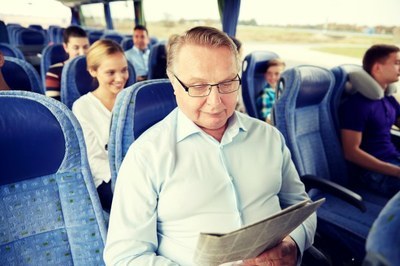 Foto de um homem idoso dentro de um ônibus lendo um jornal.