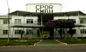 Imagem mostra a fachada principal do prédio do colégio militar em Belo Horizonte. Trata-se de um prédio de dois andares, na cor branca. No alto da fachada, há uma espécie de cobertura retangular onde está escrito CPOR - CMBH