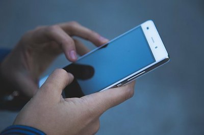 Foto mostra as mãos de um homem usando um celular. A tela está visível, mas escura: não aparece nenhuma imagem ou texto nela. 