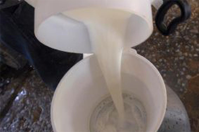 #pracegover: Fotografia mostra detalhe de um balde de leite sendo derramado dentro de um reservatório de leite em uma fazenda.