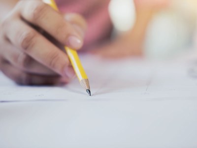 Fotografia ilustrativa de uma mão com o lápis escrevendo em uma folha.