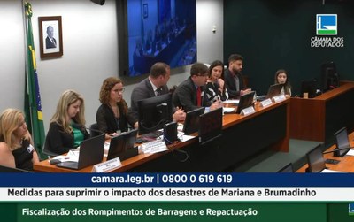 Imagem mostra uma mesa com quatro mulheres e três homens. O procurador Carlos Bruno fala ao microfone.