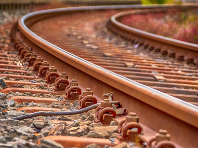 Fotografia mostra um detalhe de uma ferrovia com trilhos, e pedras em volta.
