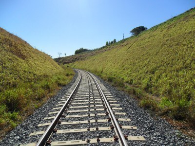 Imagem mostra trecho de uma linha de trem de ferro no meio de um vale.