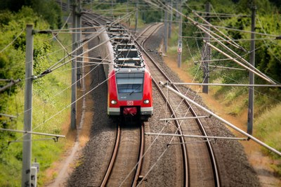 #PraCegoVer Imagem mostra a frente de uma locomotiva de trem, que está vindo por uma estrada de ferro. 