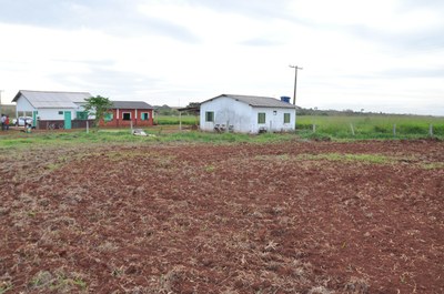 Na imagem vê-se em primeiro plano uma área de lavoura, recém gradeada, com algumas construções ao fundo, entre elas a escola da Comunidade Indígena Guyraroká