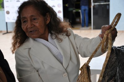 Foto mostra mulher ribeirinha, de idade avençada, segurando a alça de uma bolsa feita com palha de aguapé.