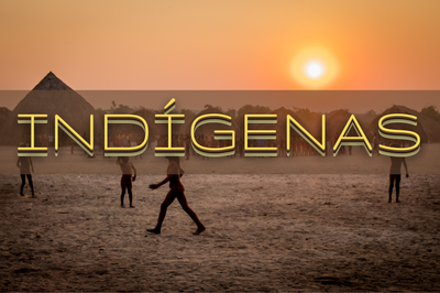 Imagem de um pôr do sol em terra indígena, quatro pessoas caminhand e ao fundo uma oca. Por cima da imagem, a palavra indígenas escrita com letras amarelas com sombra bege.