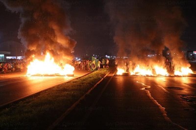 #pracegover: foto mostra pneus pegando fogo no meio de rodovia em Mato Grosso, a noite, e ao fundo uma pessoa segurando uma bandeira do Brasil