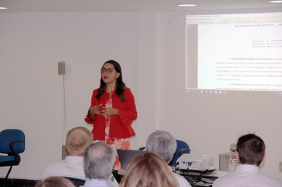 Foto mostrando uma mulher de pé, discursando diante de uma plateia