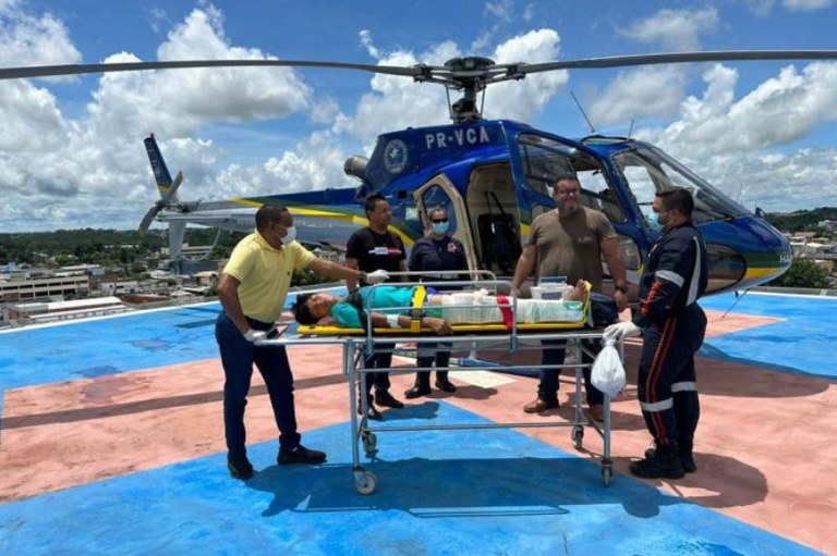 Fptp mostra um helicóptero, uma homem indígena deitado em uma maca e cinco homens ao redor