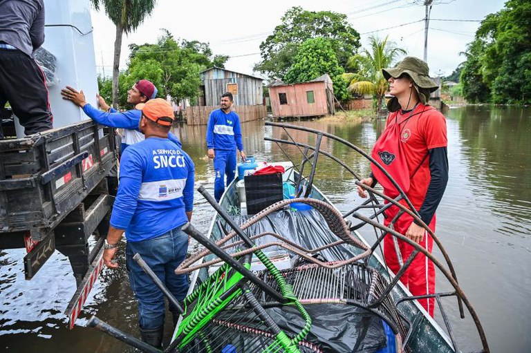 Foto mostra pessoas retirando móveis de casas alagadas na periferia de Rio Branco.