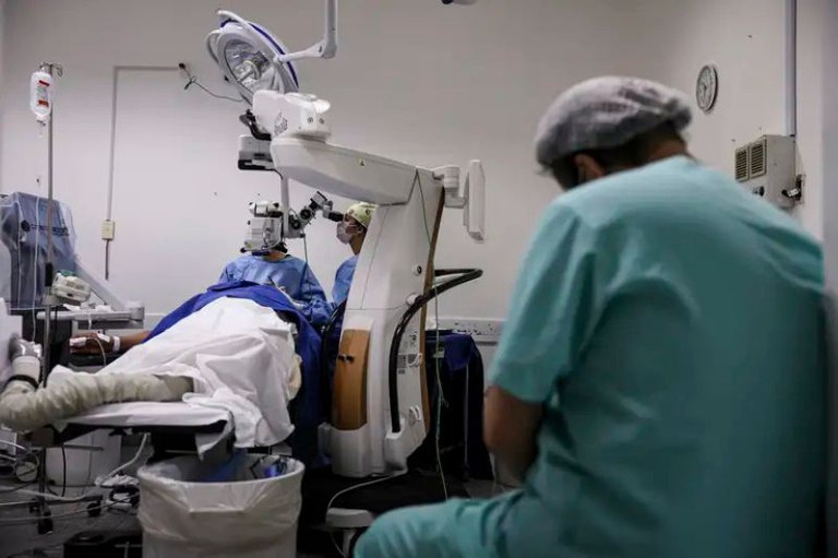 Foto mostra um paciente em um sala de cirurgia e profissionais de saúde ao redor