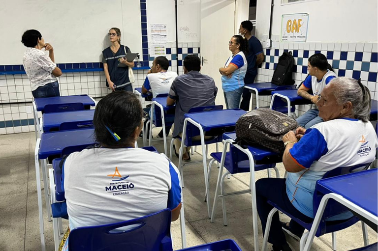 Foto da uma sala de aula. Os estudantes estão sentados ouvindo atentamente.