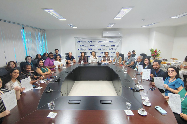 Todos os participantes do evento reunidos no entorno de uma grande mesa oval