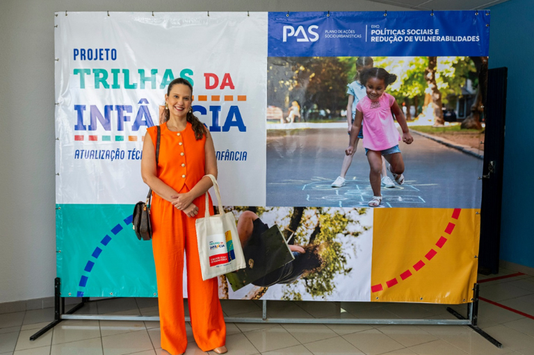 Dra Roberta Bomfim. Ao fundo, imagem do Trilhas da Infância