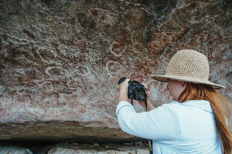 Registro fotográfico de uma mulher fotografando inscrições circulares na pedra
