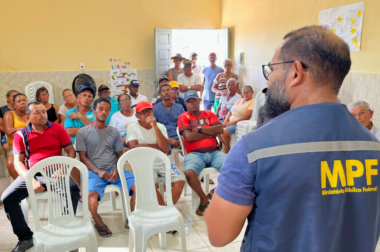 registro fotográfico da reunião com o procurador da República em destaque, no primeiro plano à direita, de costas, com o nome MPF, em letras amarelas no destaque do colete do procurador
