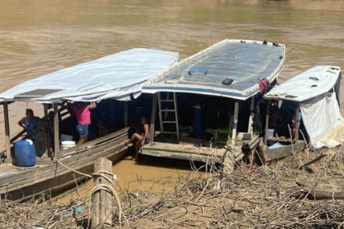 Foto mostra duas embarcações na beira do rio que abrigam de forma precária indígenas que chegam ao município de Boca do Acre