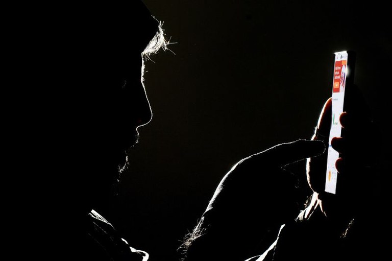 Foto escura de um homem mexendo no celular