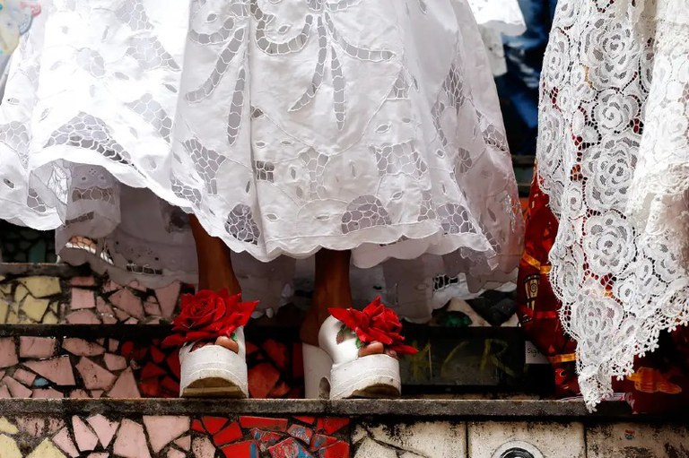 Foto mostra os pés calçados com uma sandália branca com uma grande rosa