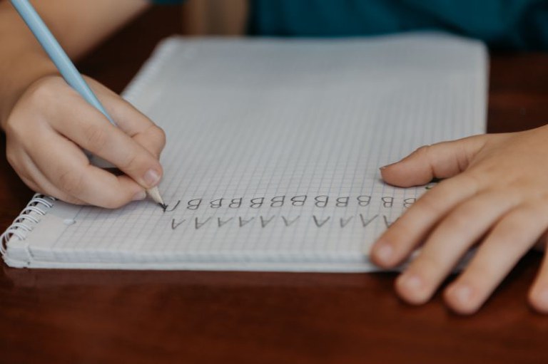 Foto em detalhe mostra uma criança escrevendo as letras no caderno